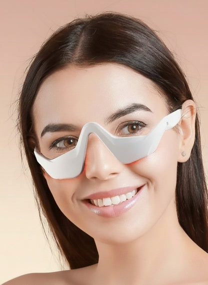 The Glow Lab EMS eye care device with red light therapy worn by a smiling woman to reduce puffiness and dark circles.