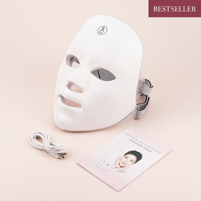 The Glow Lab white LED light therapy facial mask with USB charging cable and instruction manual on a soft background.