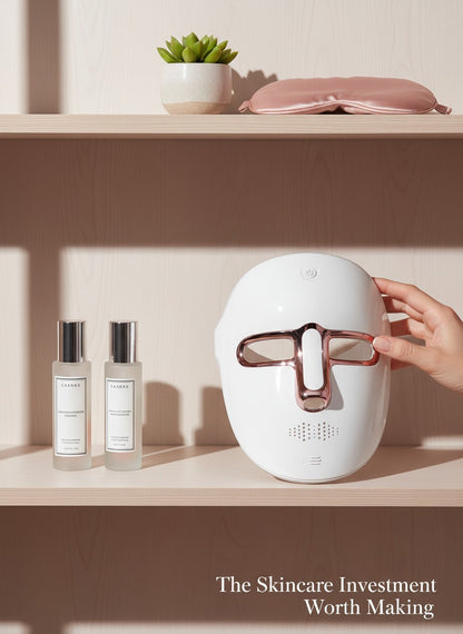The Glow Lab 7-color LED light therapy facial mask in white and rose gold, displayed on a shelf with skincare bottles.